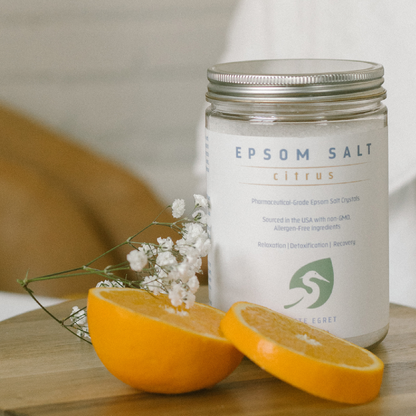 white egret's citrus orange epsom salts with essential oils for bath next to bathtub with womans legs and orange slices