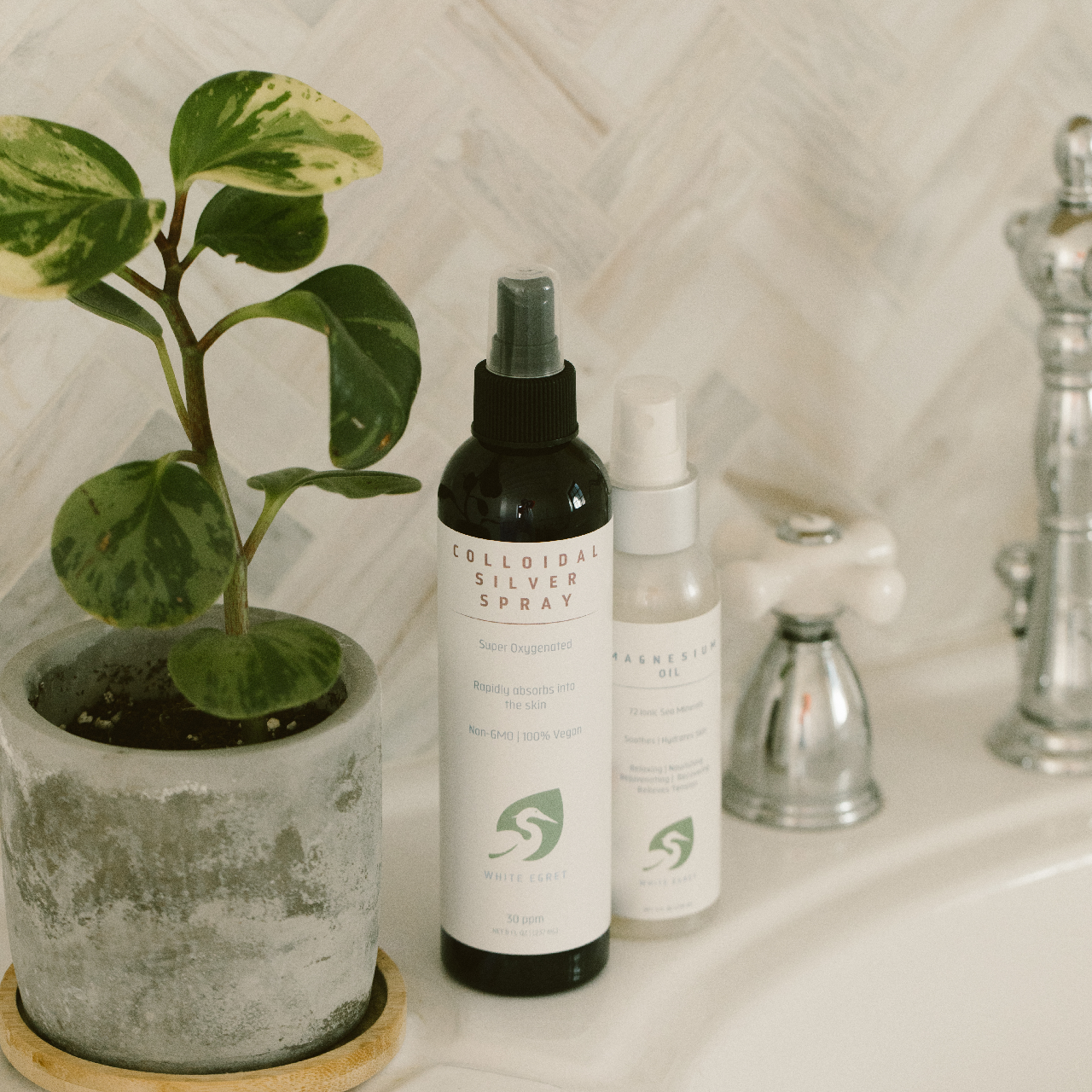 White Egret's Colloidal Silver Spray on a bathroom counter next to White Egret's Magnesium Oil with a potted plant beside it