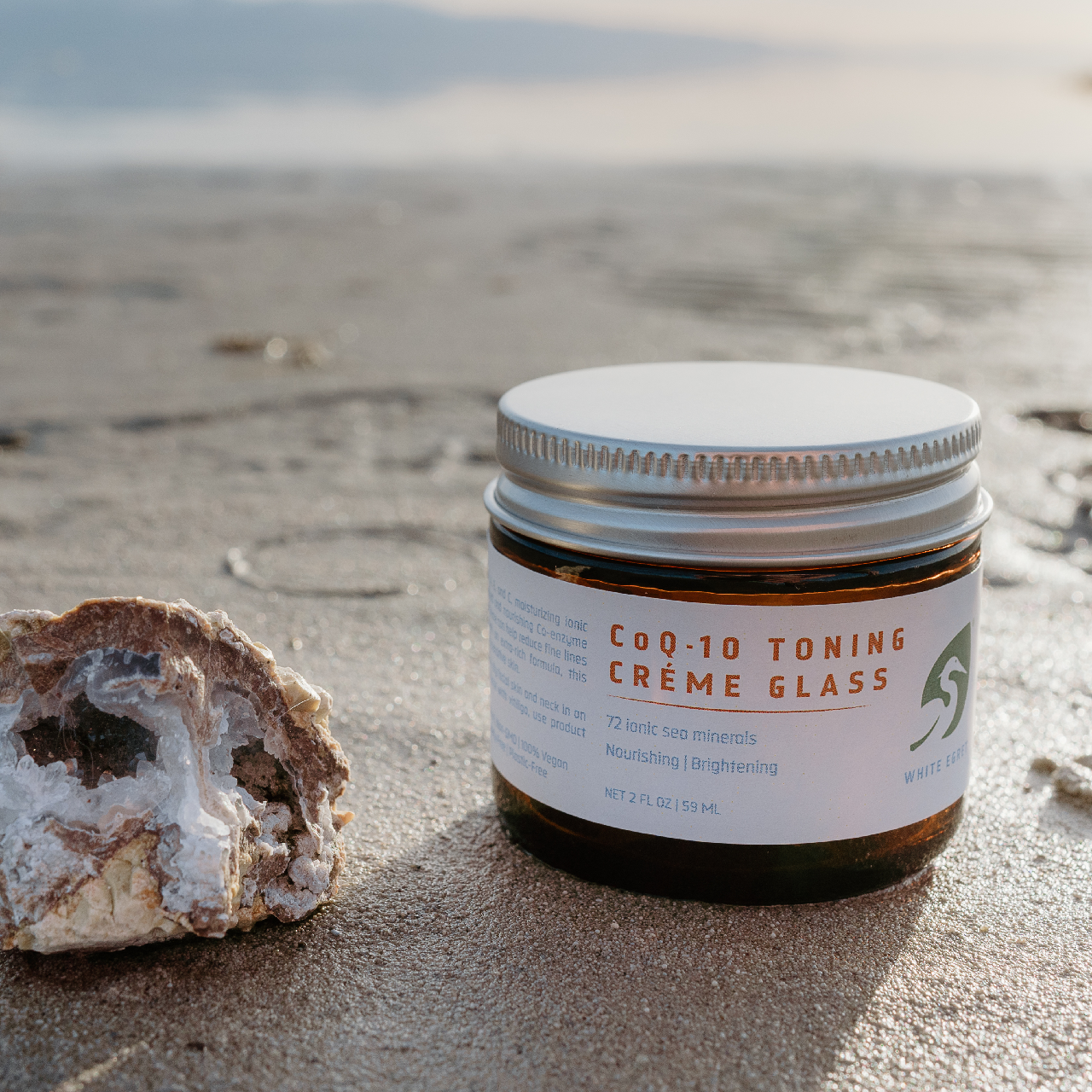 White Egret's Coq-10 Toning Creme in an amber glass jar on the shore of the Great Salt Lake next to a geode with white crystals