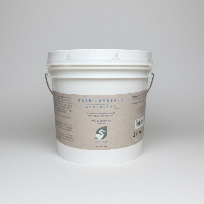 White bucket labeled 'Bath Crystals' on a wooden surface with a blurred background