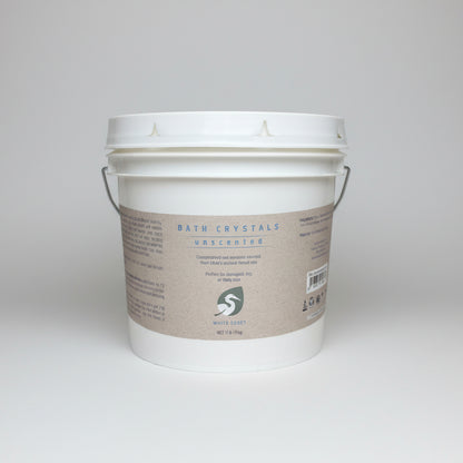 White bucket labeled 'Bath Crystals' on a wooden surface with a blurred background