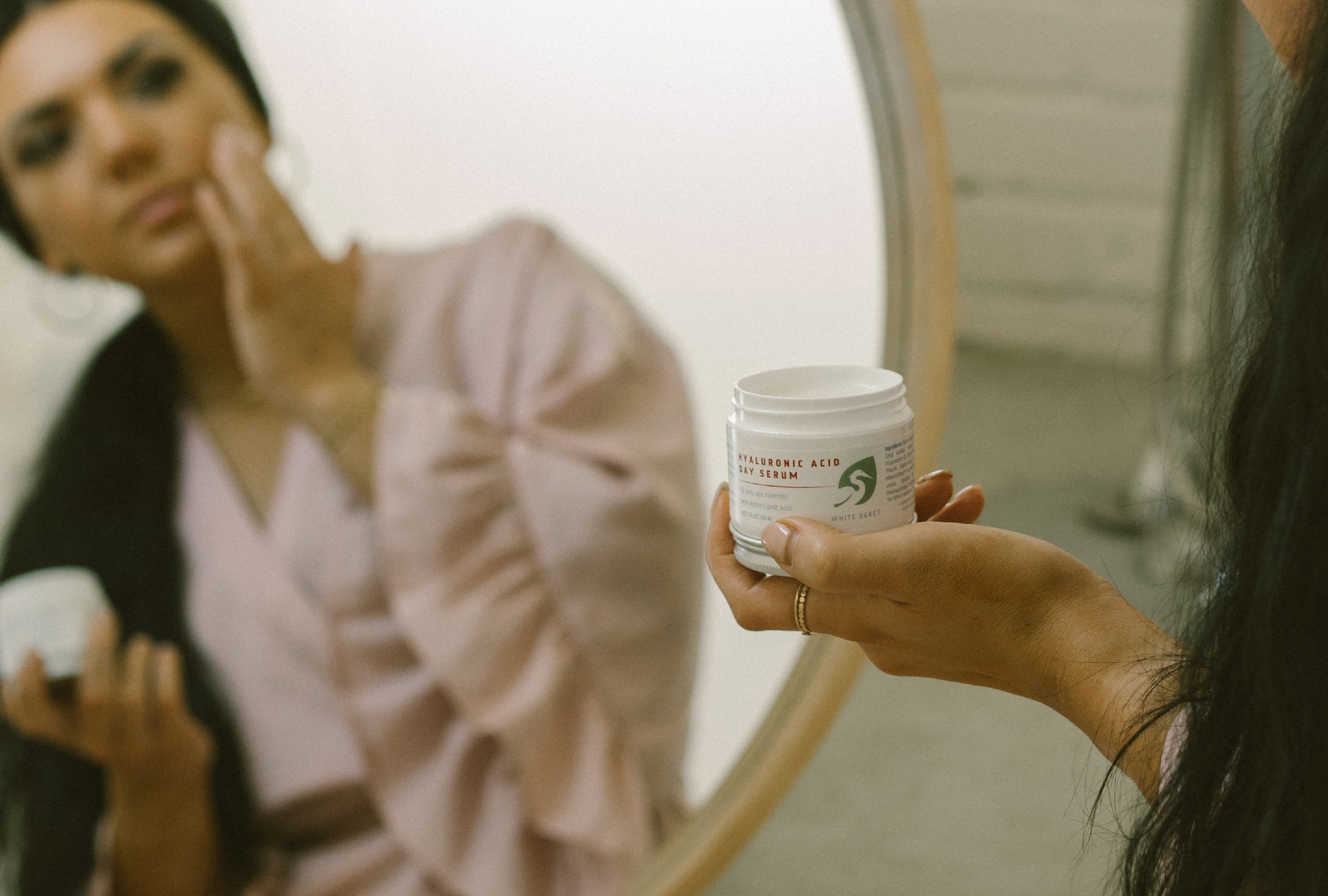 Hyaluronic Acid Day Serum being held by a woman applying product to her face looking into a mirror mineral skincare made wtih all natural ingredients